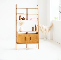 a wooden shelf with shelves and vases on it next to a window in a white room