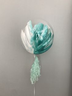 a green and white balloon with tassels hanging from it's side against a gray wall