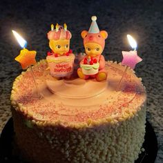 two teddy bears sitting on top of a birthday cake with candles in the shape of stars