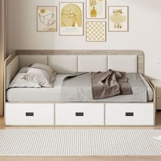 a white bed with drawers underneath it in a room next to pictures on the wall