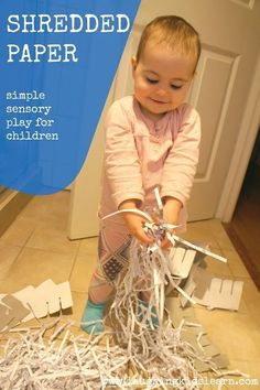 a baby playing with shredded paper on the floor