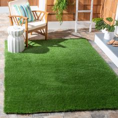 a green rug on the ground with a chair and potted plant