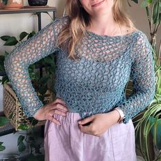 a woman standing in front of a potted plant wearing a crochet top