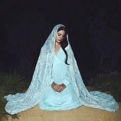 a woman sitting on the ground wearing a blue dress and veil with her hands in her pockets