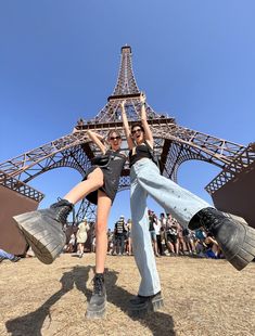 two people standing in front of the eiffel tower with their arms up and legs crossed