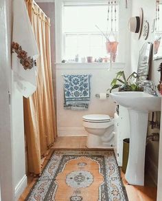 a white toilet sitting next to a sink in a bathroom under a window with yellow curtains