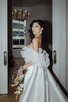 a woman in a white wedding dress holding a bouquet and looking at the camera with an open door behind her