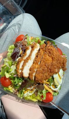 a person holding a plastic container filled with salad and chicken breast patties on top of lettuce