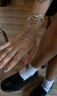 a woman's hands with tattoos and bracelets on her wrist, sitting next to a chair