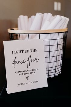 a basket filled with white napkins next to a sign that says light up the dance floor