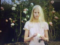 a woman standing in front of roses holding an apple