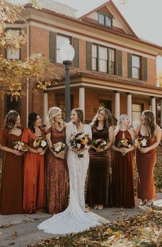 a group of women standing next to each other in front of a house with fall leaves on the ground