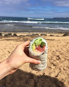 someone is holding up a sushi on the beach