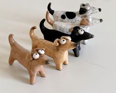 five ceramic dogs are lined up in a row on a white surface, one is black and the other is brown