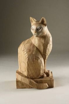 a wooden sculpture of a cat sitting on top of a piece of wood with its eyes closed