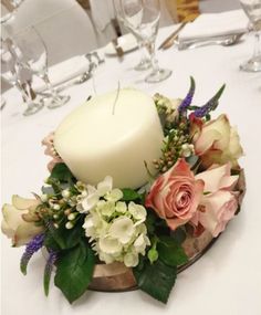 a white candle sitting on top of a wooden bowl filled with flowers and greenery