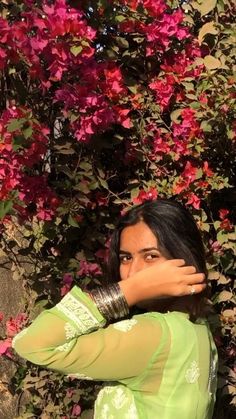 a woman standing in front of pink flowers with her hands on her face and arms behind her head