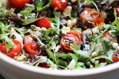 a salad with tomatoes, lettuce and other toppings in a white bowl