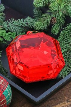 an ornament sitting on top of a black tray next to christmas tree branches