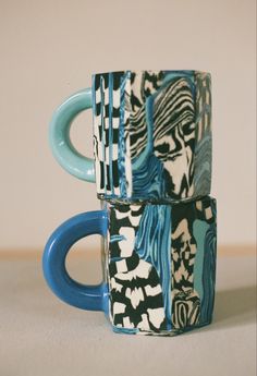 two stacked coffee mugs sitting next to each other on top of a white table