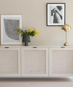 a white sideboard with two pictures on the wall and flowers in a vase next to it