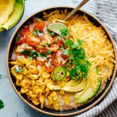 a bowl filled with mexican corn salad and topped with avocado wedges on the side