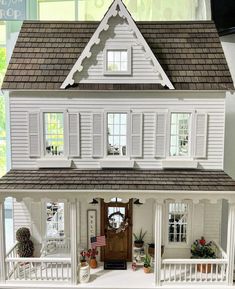 a doll house with white sidings and brown shingles on the front door, porch, and second story