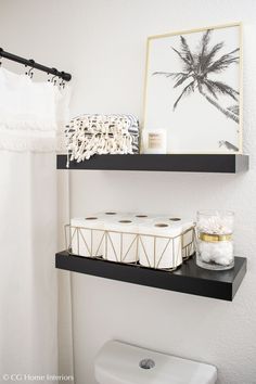 two black shelves above a toilet in a white bathroom with pictures on the wall behind them