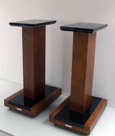 two wooden speakers sitting side by side on top of a white table with black bases