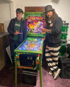 two men standing next to each other in front of a pinball machine