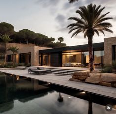 a large pool surrounded by palm trees next to a house with glass doors and windows