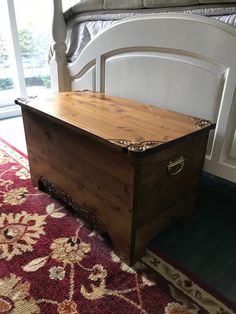 a large wooden chest sitting on top of a rug in front of a white bed