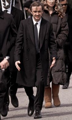 a man in a suit and tie walking down the street with other people behind him