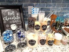 a counter topped with lots of different types of candies and desserts next to a sign that says hot chocolate bar