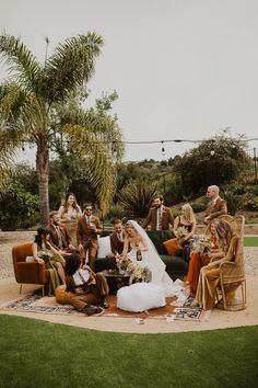 a group of people sitting around each other on top of a grass covered field with palm trees