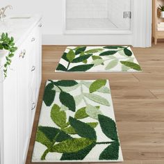 two bathroom rugs with green leaves on them in front of a bathtub and sink