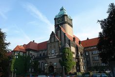 an old building with a clock tower on the front and side of it, surrounded by trees