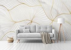 a white couch sitting in front of a wall with gold leaves on it and a lamp next to it