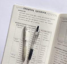 two pens sitting on top of an open book next to another pen and paper with writing