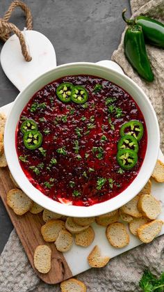 a white bowl filled with cranberry sauce surrounded by crackers and green peppers