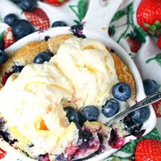 a bowl filled with ice cream and blueberries on top of a table next to strawberries