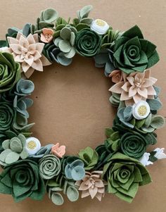 a close up of a wreath made out of felt flowers and green leaves on a brown background