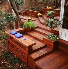 a wooden deck with planters and pillows on the steps leading up to it's entrance