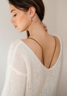 a woman with her back to the camera wearing a white sweater and gold hoop earrings