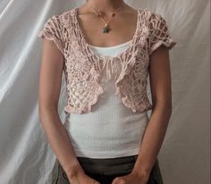 a woman standing in front of a white backdrop wearing a pink crochet top