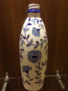 a white vase with blue and yellow flowers on it sitting on a glass shelf in front of a wooden wall