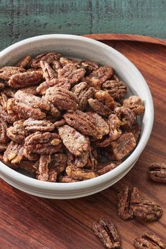 a white bowl filled with pecans sitting on top of a wooden cutting board