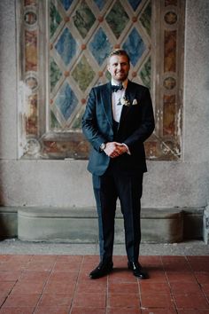 a man in a tuxedo standing next to a wall with stained glass windows