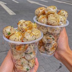 two plastic cups filled with food sitting on top of a street side walk next to a person's hand