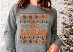 a woman standing in front of a christmas tree wearing a sweater with the words go cleveland printed on it